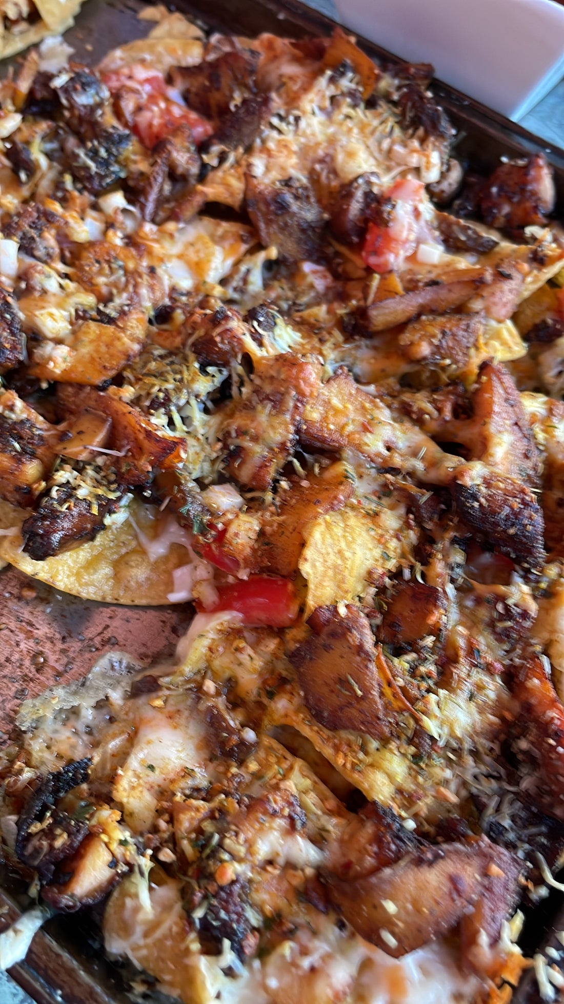 a pan of tortilla chips covered in melted cheese, chunks of chicken, spices and fresh tomatoes.